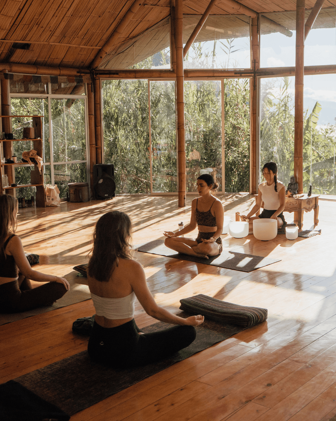 Women meditating with crystal singing bowls in a sunlit bamboo yoga shala on an ASHA retreat